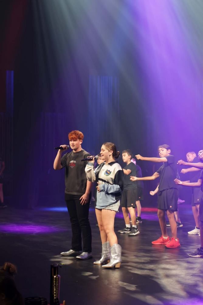 A group of people are standing on a stage singing into microphones.