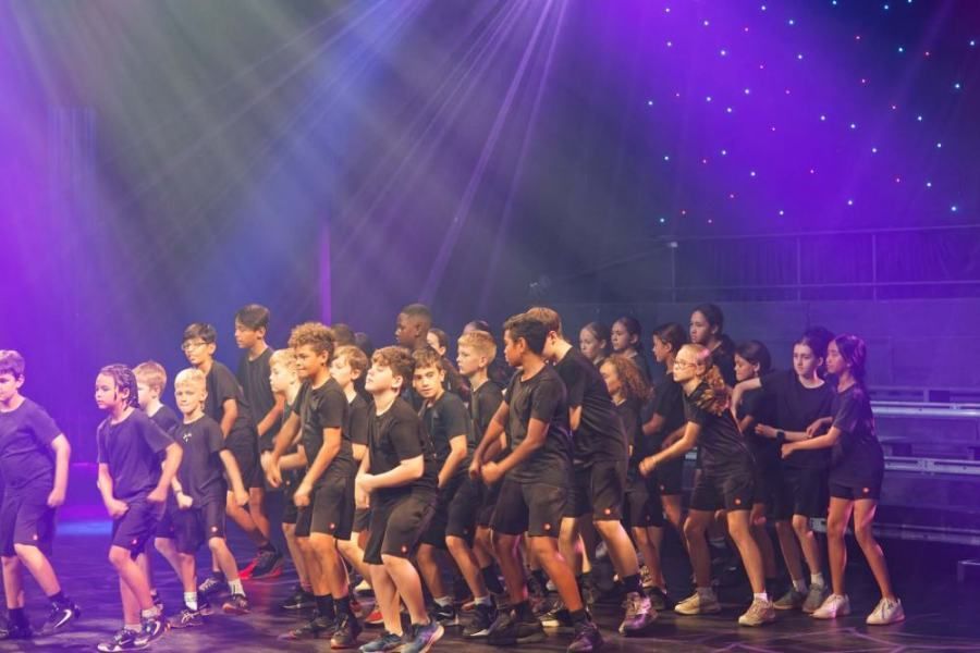 A group of children are standing on a stage in front of a purple light.