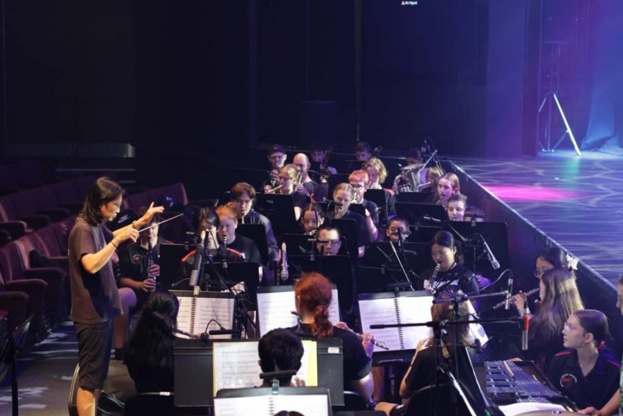 A man is standing in front of an orchestra on a stage.