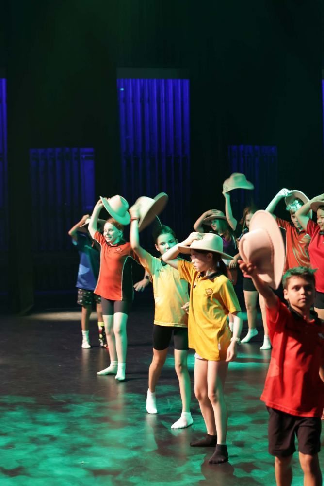 A group of children are dancing on a stage while wearing cowboy hats.