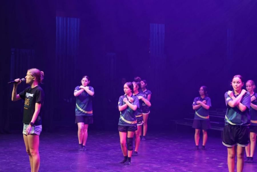 A woman is singing into a microphone while a group of girls are dancing on a stage.