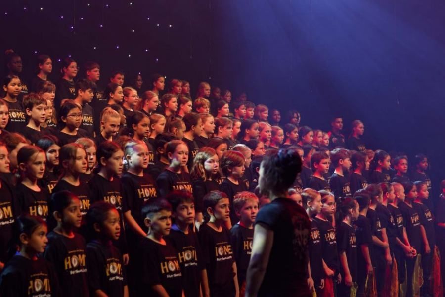 A large group of children are standing in a line on a stage.