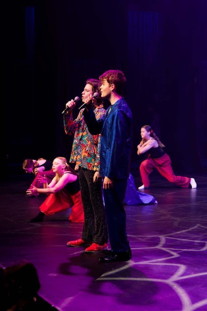 A group of people are standing on a stage singing into microphones.