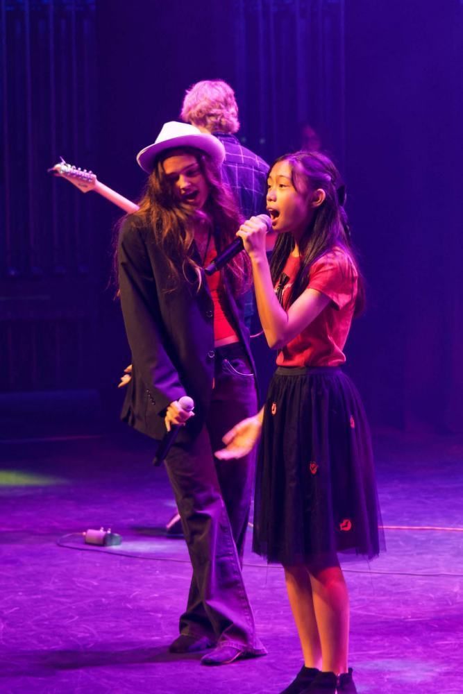 A woman and a girl are singing into microphones on a stage.