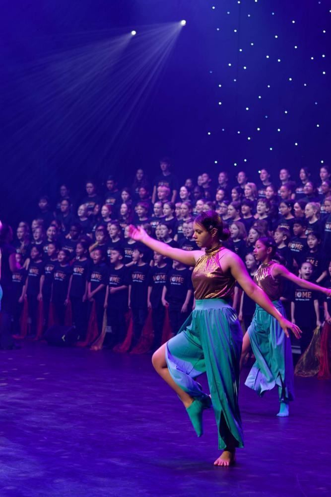 A group of women are dancing on a stage in front of a choir.
