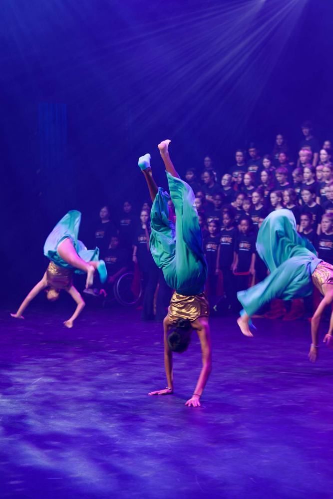 A group of dancers are doing a handstand on a stage in front of a crowd.