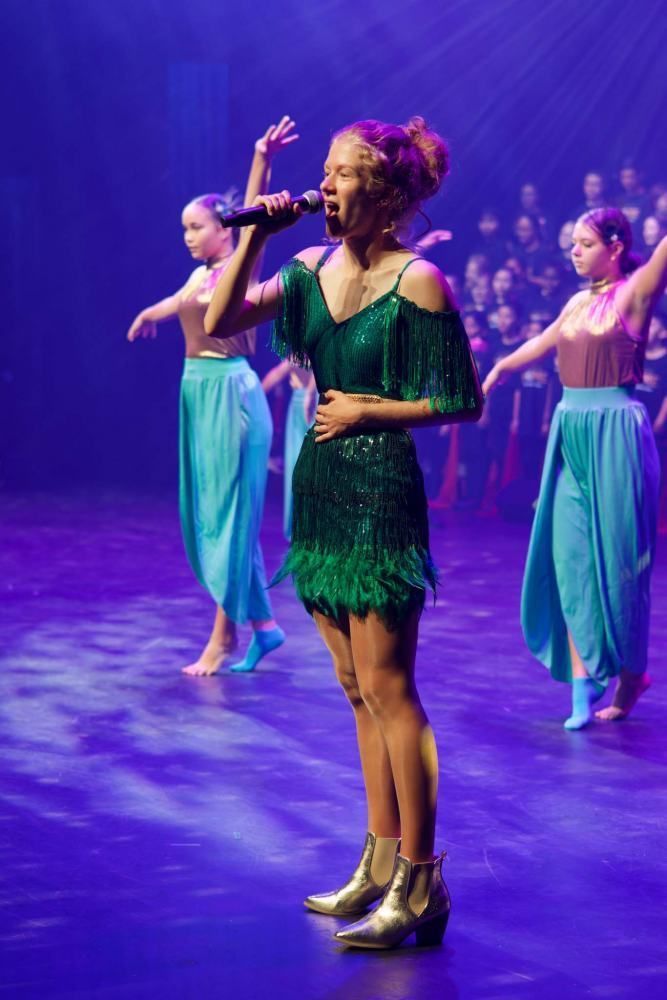 A woman in a green dress is singing into a microphone on a stage.