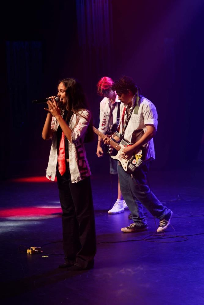 A woman is singing into a microphone while two men play guitars on stage.