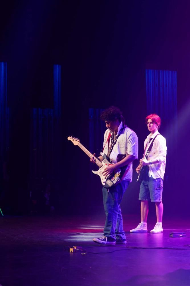 Two men are playing guitars on a stage in a dark room.