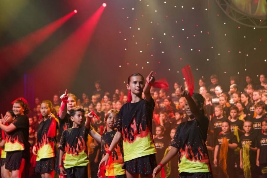A group of children are dancing on a stage in front of a crowd.