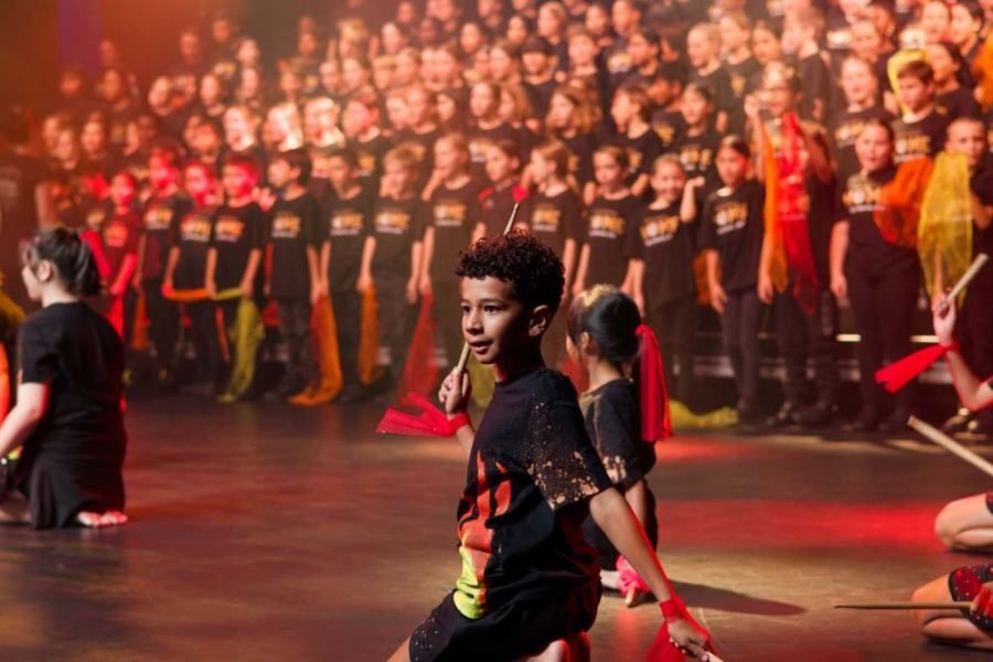 A group of children are dancing on a stage in front of a large choir.