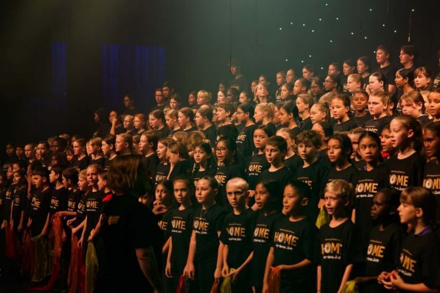 A large group of children are singing in a choir on a stage.