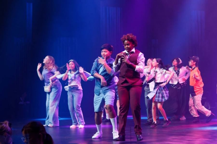 A group of people are dancing on a stage with purple lights.