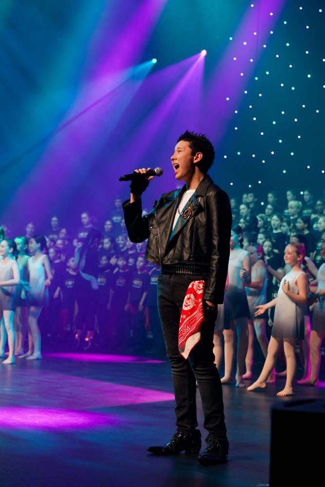 A man is singing into a microphone on a stage in front of a choir.