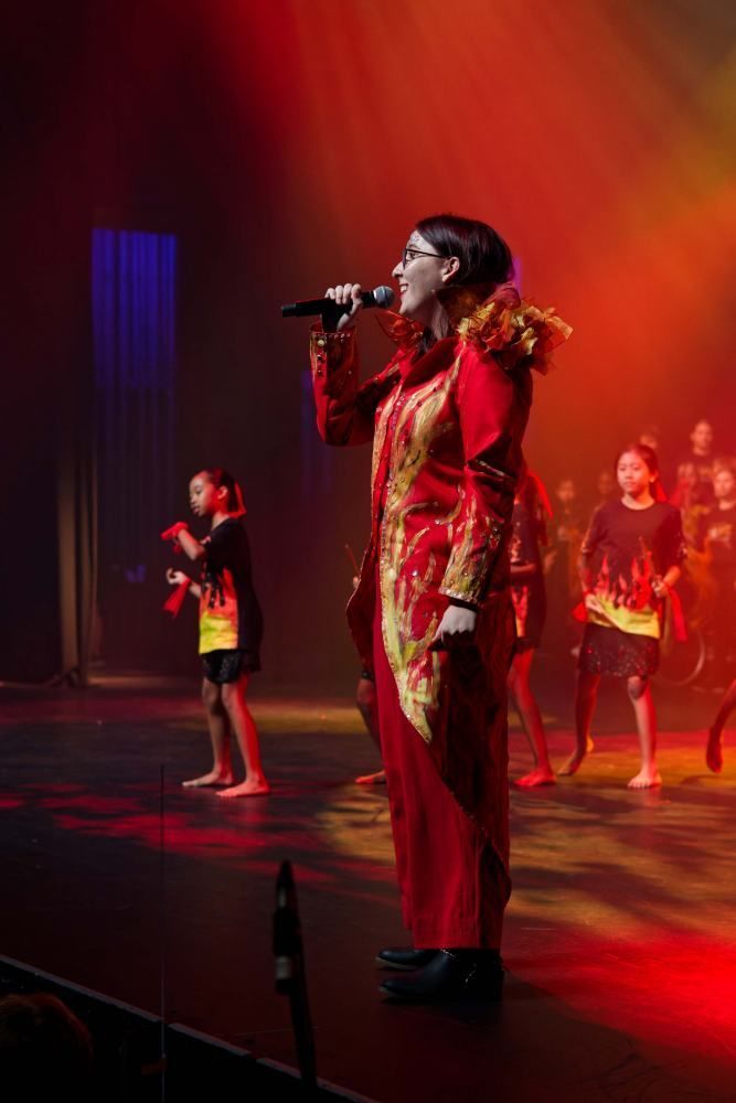 A woman in a red dress is singing into a microphone on a stage.