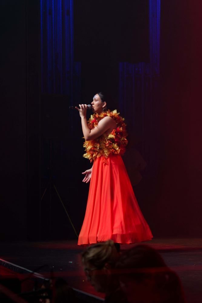 A woman in a red dress is singing into a microphone on a stage.