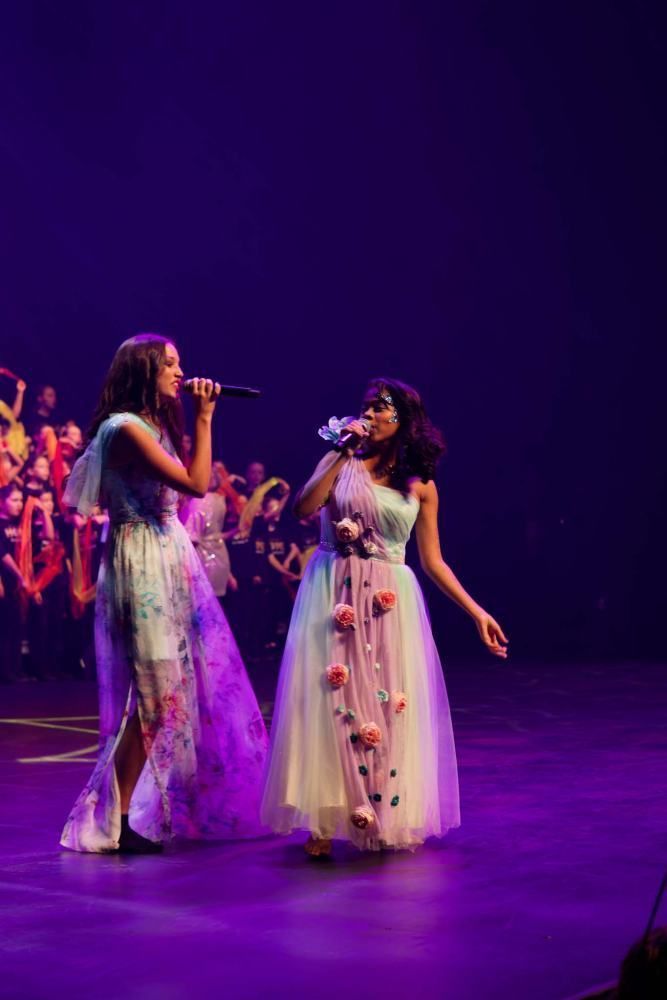 Two women are singing into microphones on a stage.