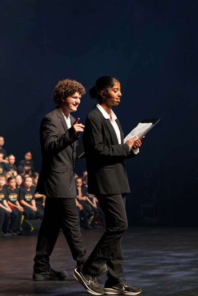A man and a woman are standing on a stage holding papers.