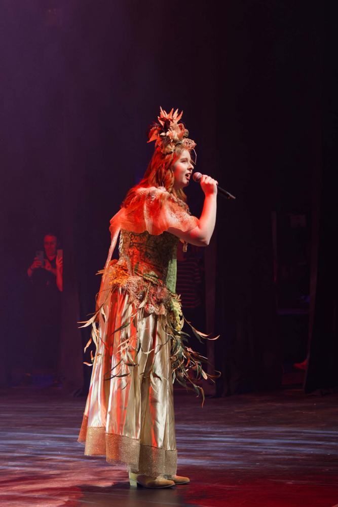 A woman in a costume is singing into a microphone on a stage.