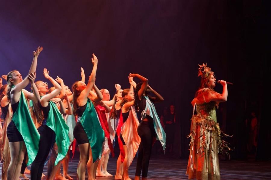 A group of dancers are performing on a stage with a woman singing into a microphone.