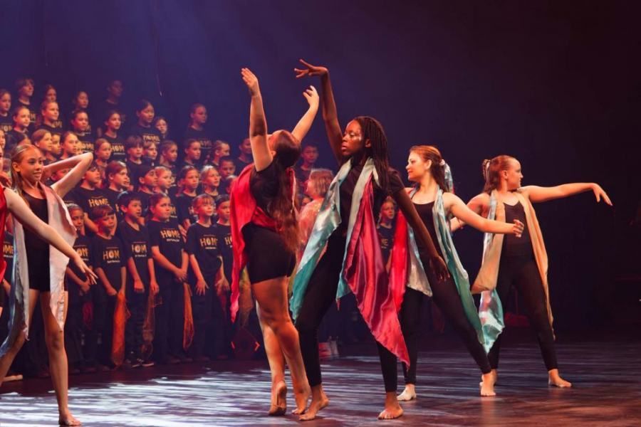 A group of young girls are dancing on a stage in front of a choir.