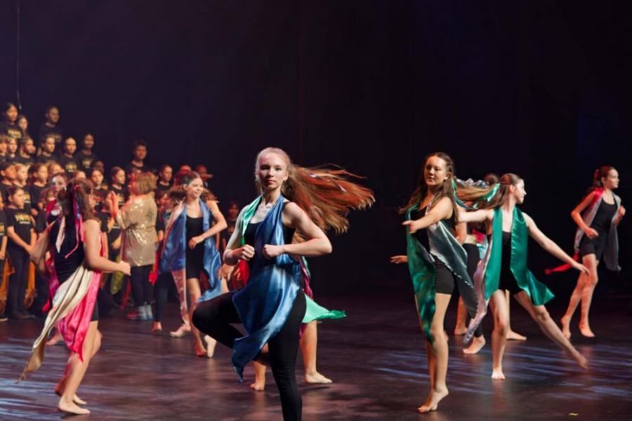 A group of young girls are dancing on a stage in front of a choir.