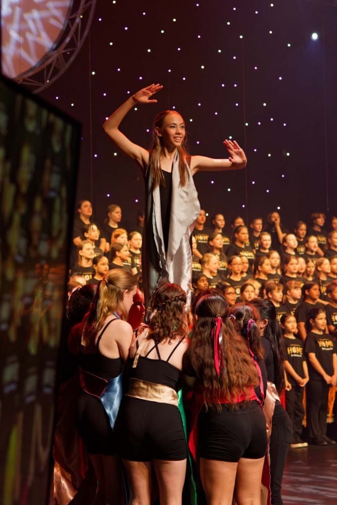A girl is standing on a stage in front of a choir.