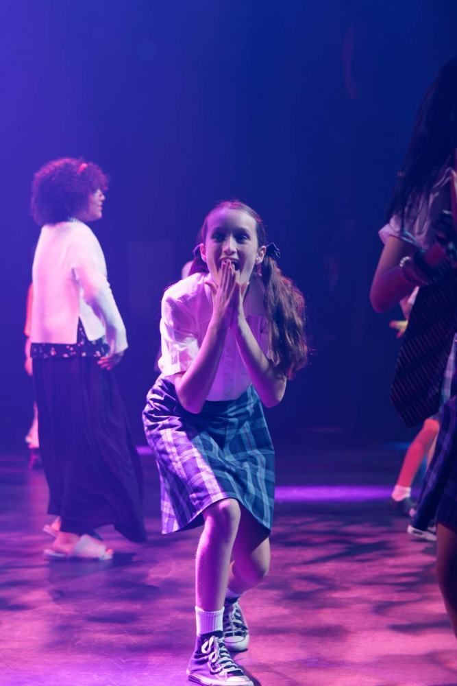 A group of young girls are dancing on a stage in a dark room.