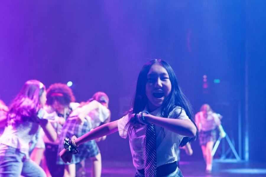 A group of young girls are dancing on a stage with purple lights.