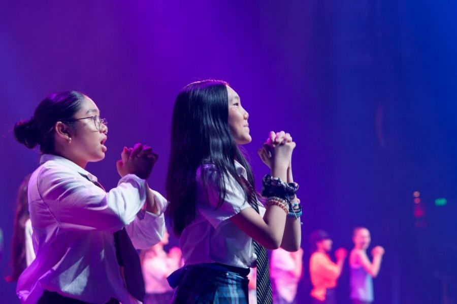 Two girls are standing next to each other on a stage in front of a microphone.