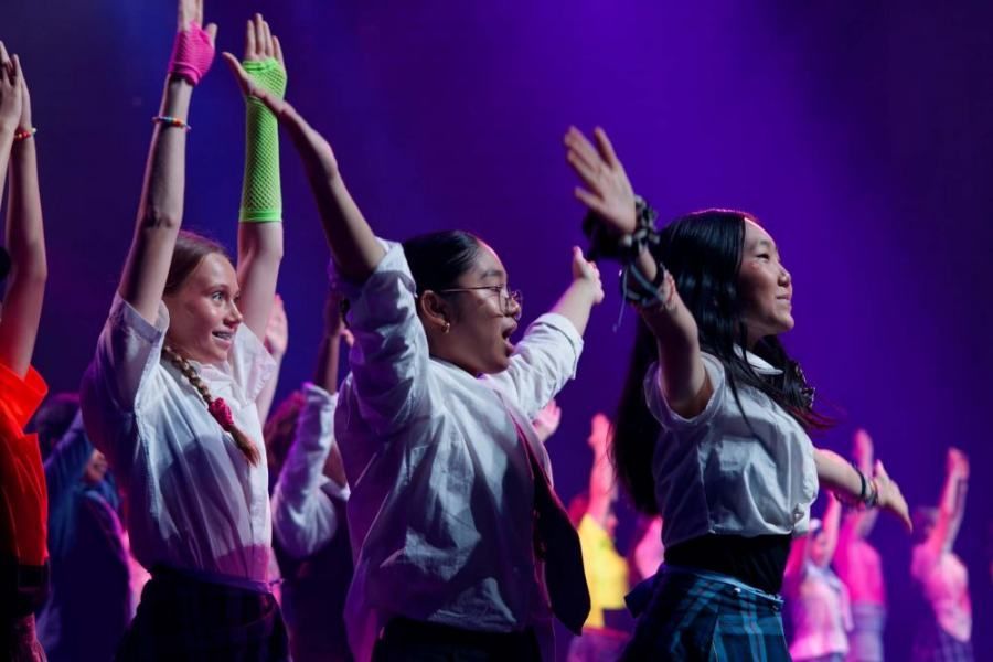 A group of young women are dancing on a stage with their arms in the air.