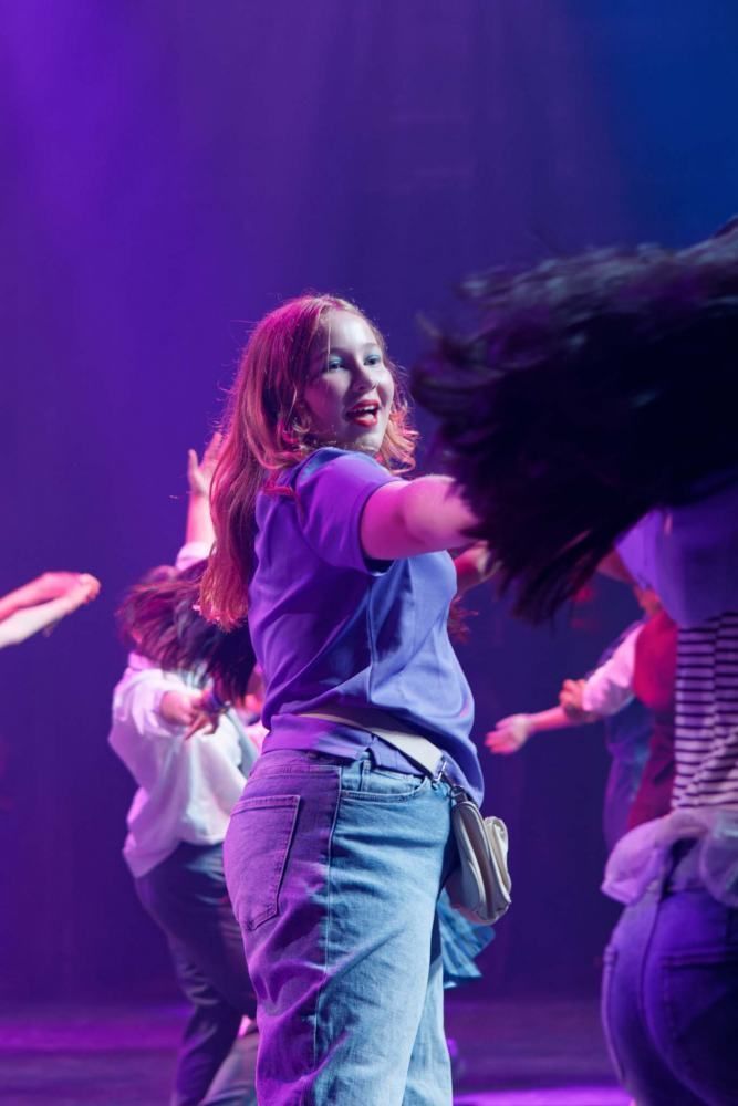 A group of people are dancing on a stage in front of a purple light.