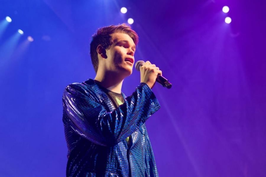 A young man is singing into a microphone on a stage.