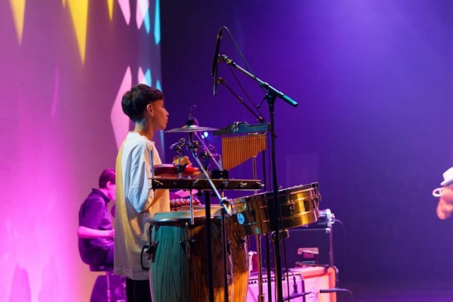 A man is playing drums on a stage in front of a microphone.