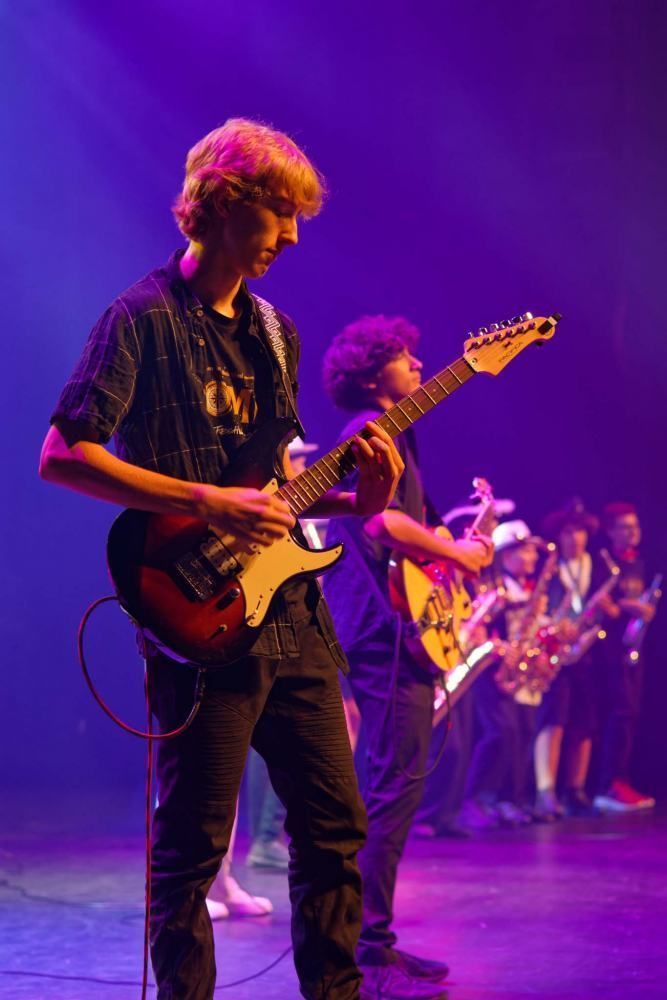 A man is playing a guitar on a stage in front of a band.