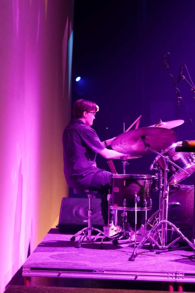 A man is playing drums on a stage with purple lights