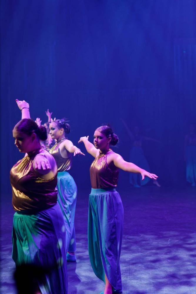 A group of women are dancing on a stage with their arms outstretched.