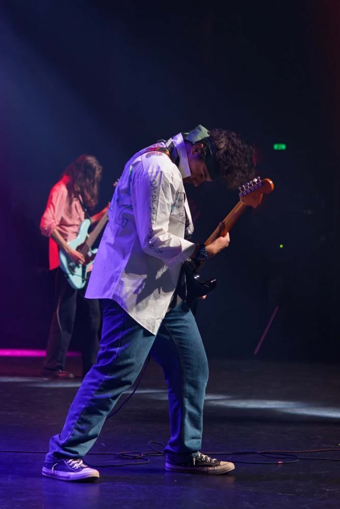 A man is playing a guitar on stage in a dark room.