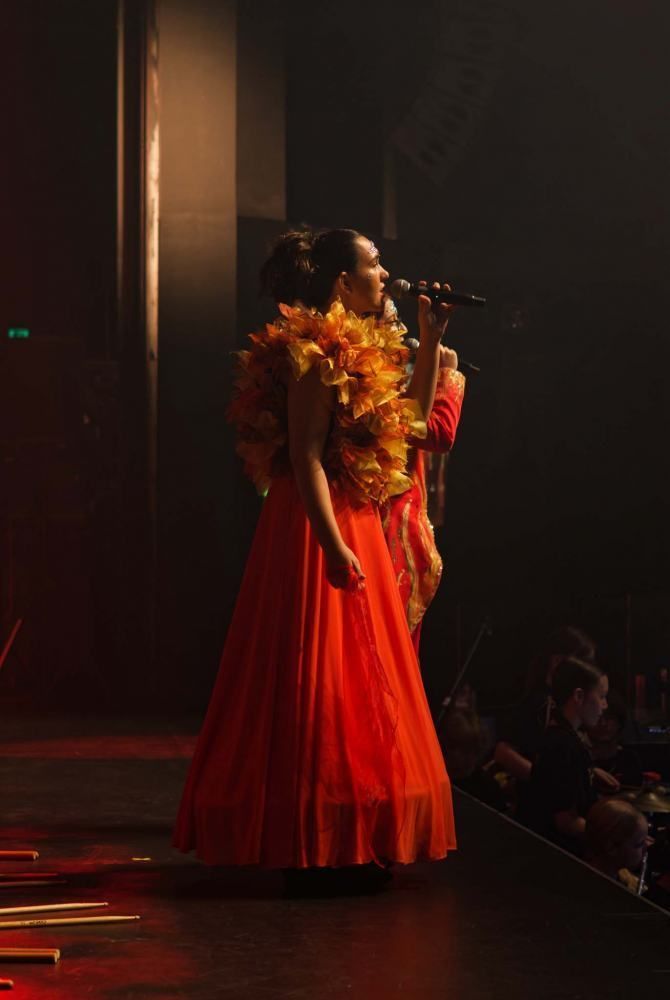 A woman in a red dress is singing into a microphone on a stage.