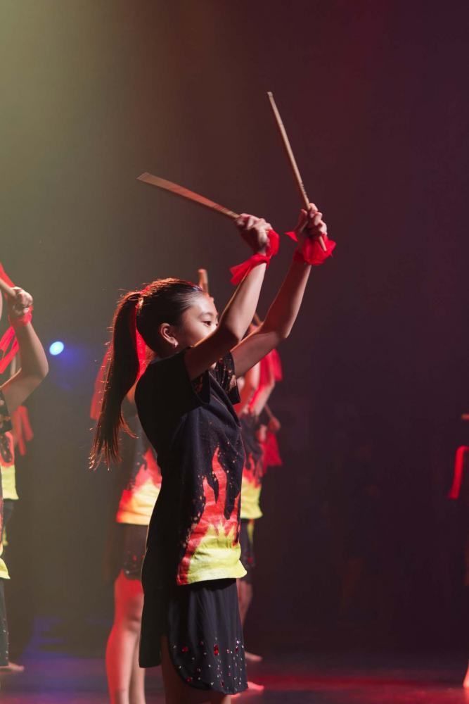 A girl in a black dress is holding a stick in the air