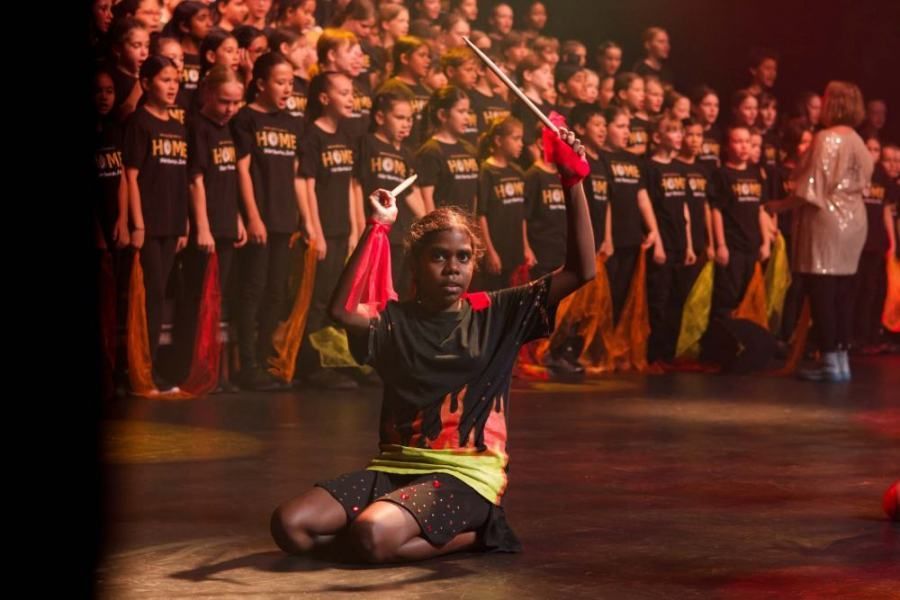 Children playing drums at a performance with choir in the background