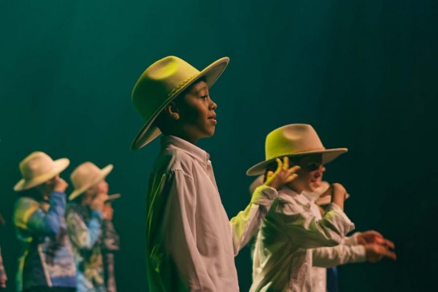 A group of children wearing cowboy hats are singing into microphones on a stage.