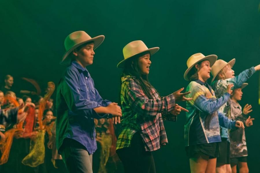 A group of children wearing cowboy hats are dancing on a stage.