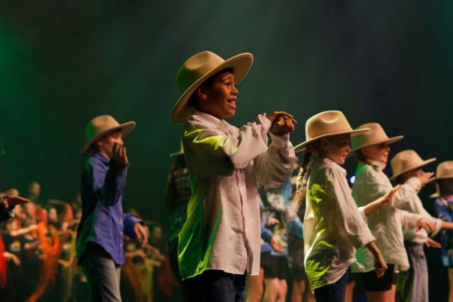 A group of children wearing cowboy hats are dancing on a stage.