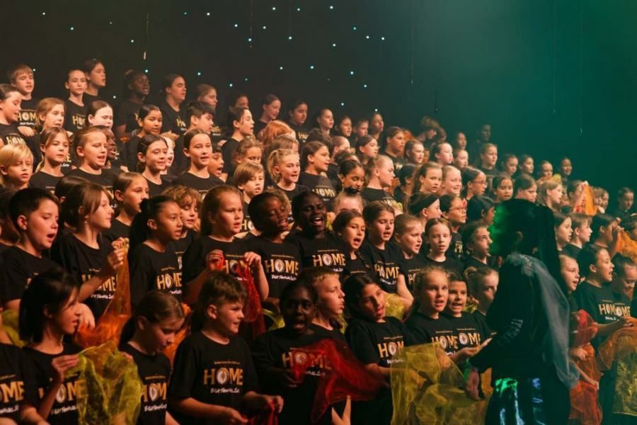 A large group of children are singing in a choir on a stage.