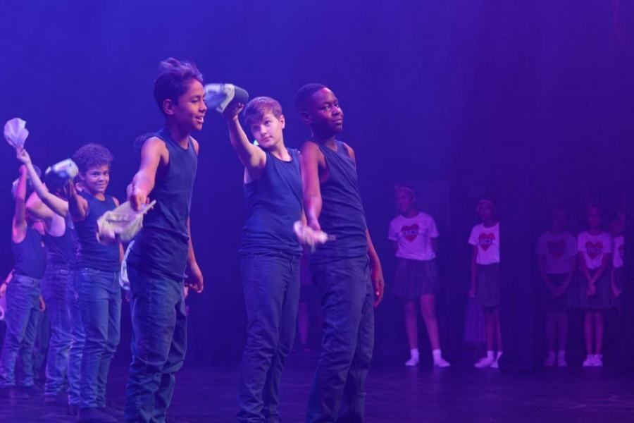 A group of children are standing on a stage in front of a purple light.