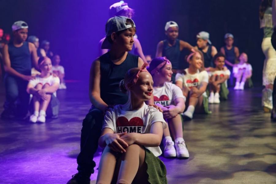 A group of children are sitting on the floor on a stage.