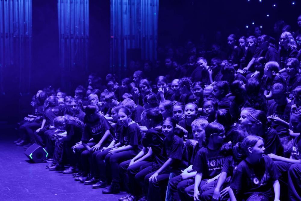 A large group of people are sitting on the floor in a dark room.