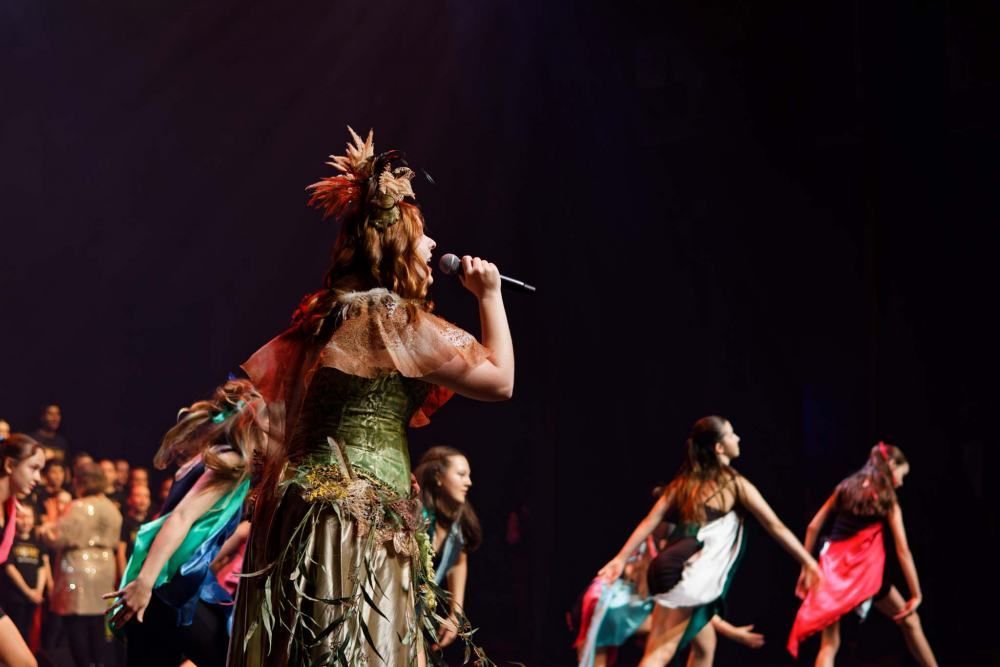 A woman in a green dress is singing into a microphone on a stage.