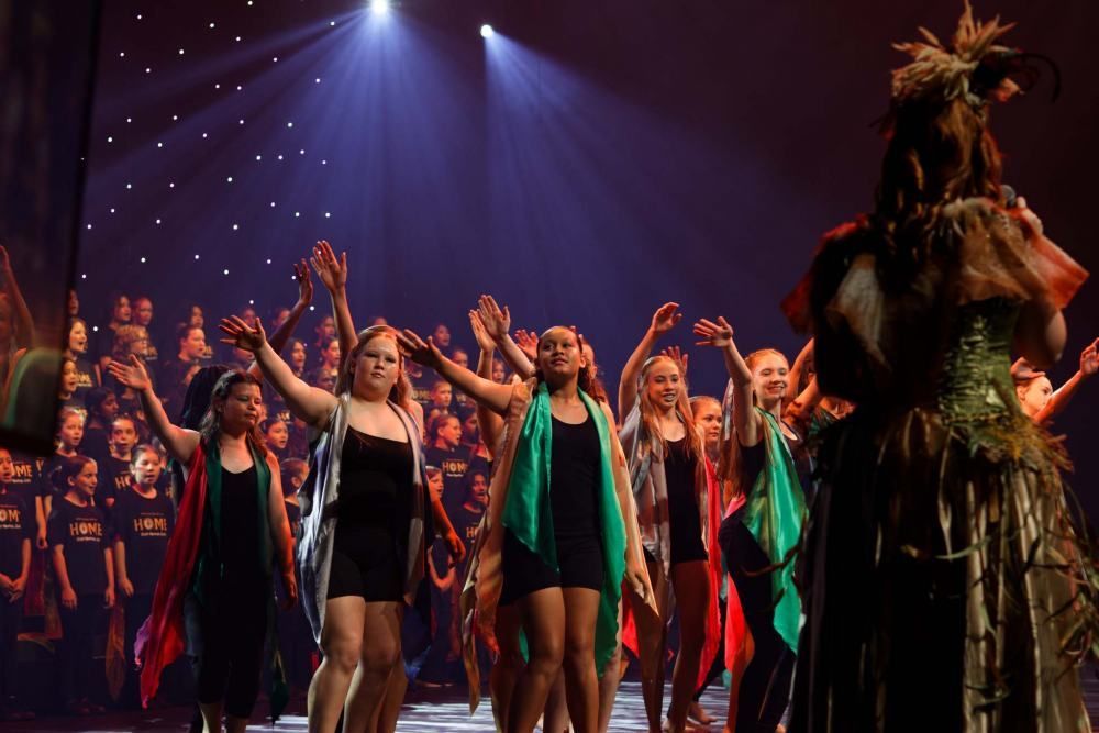A woman is standing in front of a group of dancers on a stage.